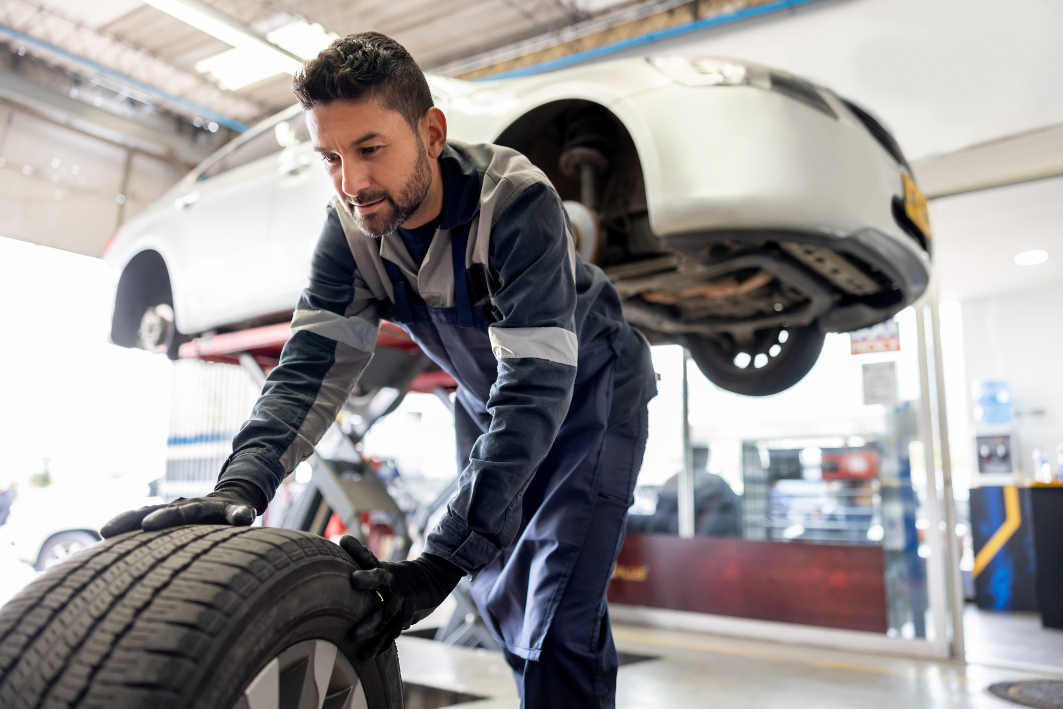 Happy Latin American mechanic changing a flat tire on a car at an auto repair shop